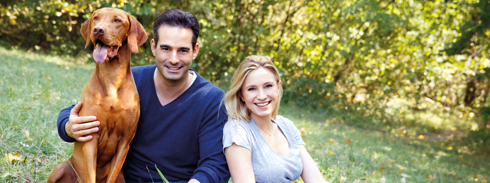 Katharina and Stefan Miklauz sitting in a meadow with their dog Pluto.