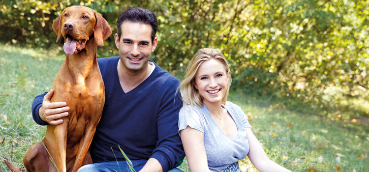 Katharina and Stefan Miklauz sitting in a meadow with their dog Pluto.