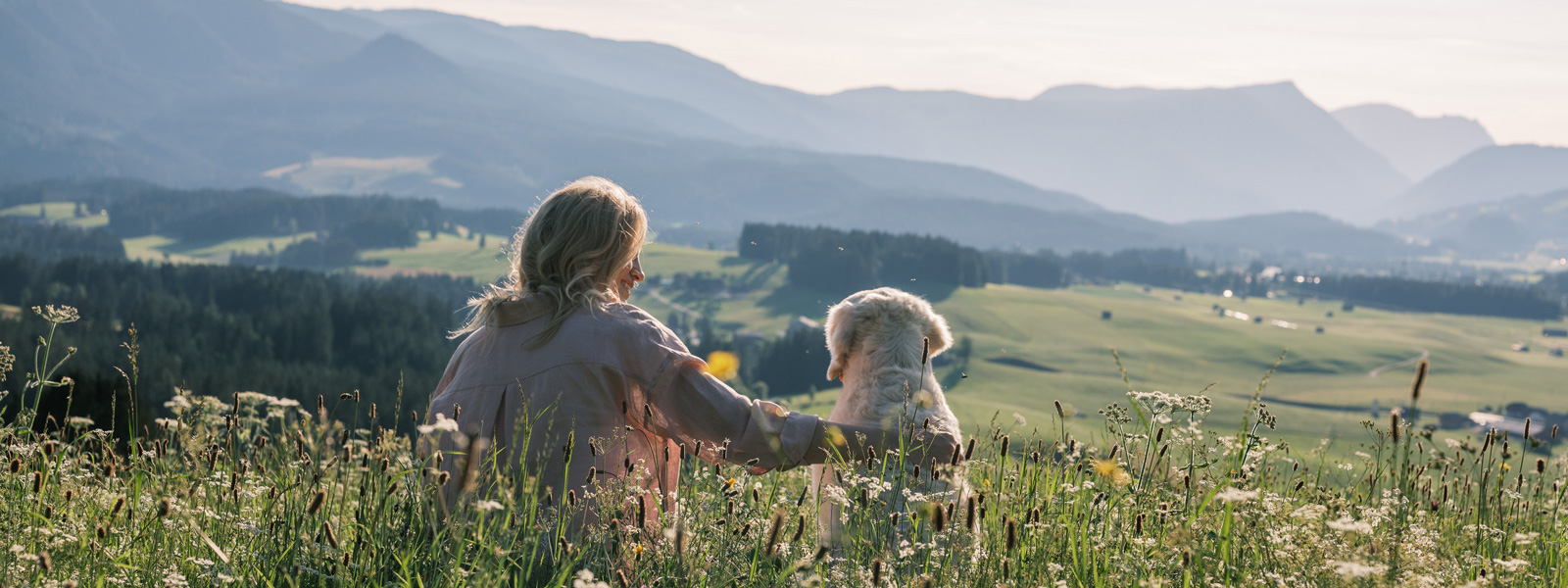 Katharina and Nala sit in a meadow and look down a hill