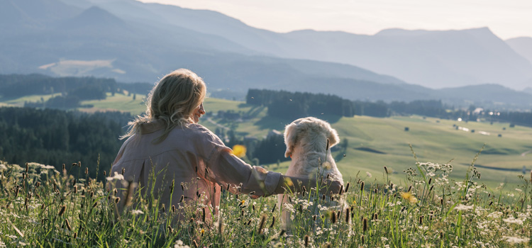 Katharina and Nala sit in a meadow and look down a hill